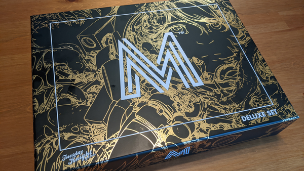 Mothership's Deluxe Set box, black and gold, sitting on a wooden table.