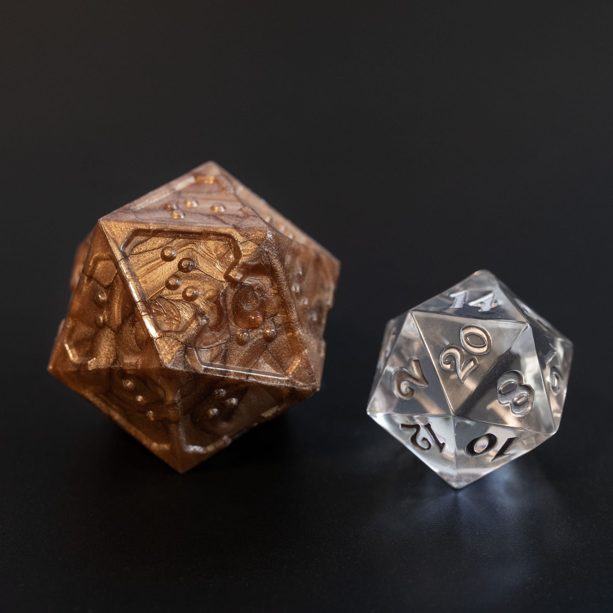 Acrylic braille d20 next to a standard sized clear acrylic d20 for comparison. The braille d20 is about twice the size.