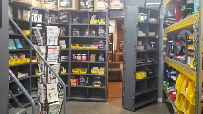 One gray shelf in a storage room full of yellow crates opens to reveal a secret room beyond.