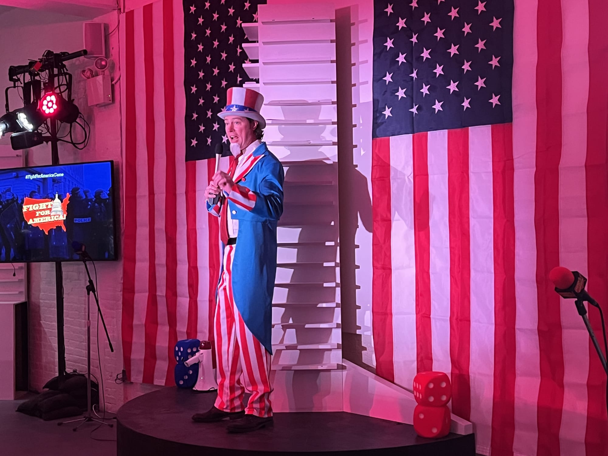 a man dressed as Uncle Sam on a small platform, flanked by American flags and television screens,