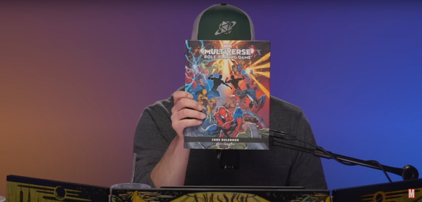 Troy Lavelle sitting behind a DM screen, holding the Marvel Multiverse Role Playing Game in front of his face