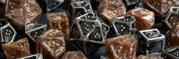 Close up view of a pile with multiple braille polyhedral dice. The sets are metallic bronze acrylic and silver hollow metal.