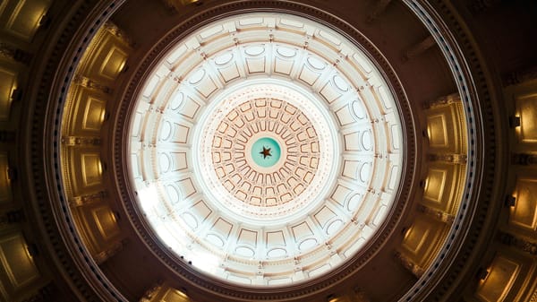 Interior view of the Texas Capitol building's dome in Austin. Golden light flanks a white center with a gold star on blue.