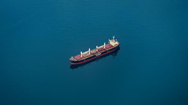 Top-down view of a blue-and-red cargo ship in the middle of the ocean. Only water is visible around it.